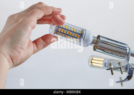 Replacing lamps in ceiling light, close-up of female hand is screwing  LED corn lamp into lampholder. Stock Photo