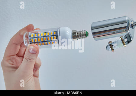 Replacing lamps in ceiling lighting device with LED corn-type lamps, electrician's hand close-up. Stock Photo