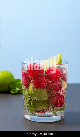 Raspberry lemonade with lime and mint in a glass. Non-alcoholic raspberry refreshment drink. Raspberry mojito in a glass with mint and lime. Stock Photo