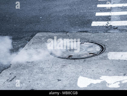 Manhole cover with steam coming out around it Stock Photo