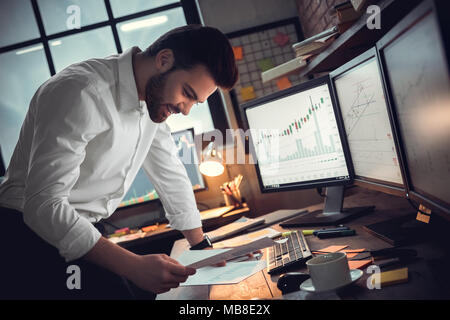 Young bearded man trader at office standing near table looking at documents smiling cheerful growth Stock Photo
