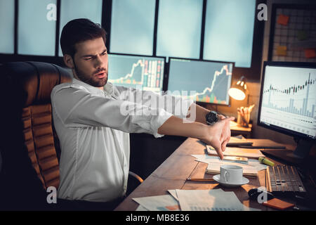 Young bearded man trader at office sitting at table stretching tired looking at screen Stock Photo