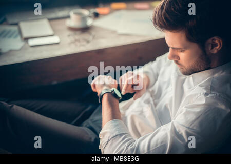 Young bearded man trader at office sitting at table checking time top view close-up Stock Photo