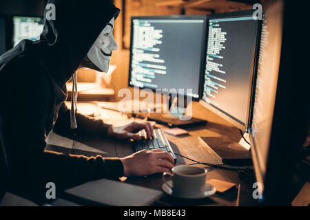 Young man financial hacker at office sitting at table wearing mask stealing information Stock Photo