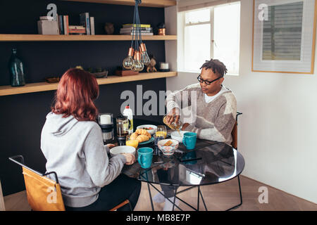 Young couple having breakfast together at home. African man with girlfriends sitting around dining table eating breakfast together. Stock Photo