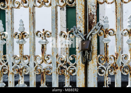 Rusty iron door with padlock attached to a chain, closing the door. Iron door worked with details. Padlock on the right. Stock Photo