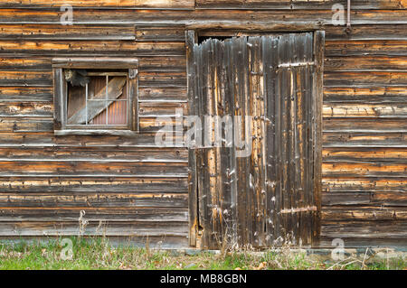 Side of Barn showing Distressed Board Door with Corrugated Metal and Wood in Window. Stock Photo