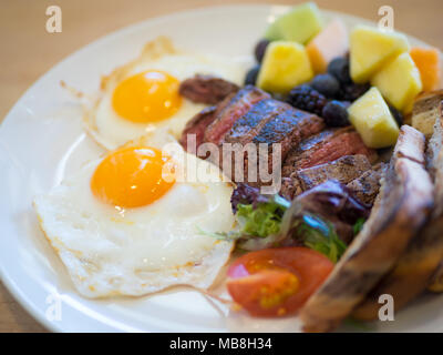 Steak eggs for breakfast at Hometown Diner in Saskatoon, Canada. Medium rare flank steak, sunny side up eggs, marble rye toast, and fruit pictured. Stock Photo