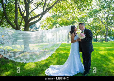 Newlywed couple facing each other holding hands, bride and groom with veil blowing in the wind Stock Photo