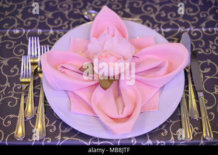 Formal table setting with silverware placed in the order of use, and elegantly wrapped napkin in the shape of a flower on top of white china Stock Photo