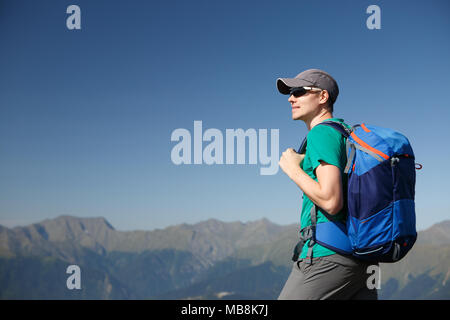 Image of tourist man in sunglasses with backpack against backdrop of picturesque mountains in summer afternoon Stock Photo