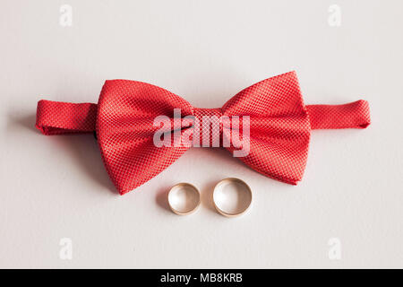 Closeup top view of elegant stylish red male bowtie and two golden rings isolated. Preparation for wedding day concept. Horizontal color photography. Stock Photo