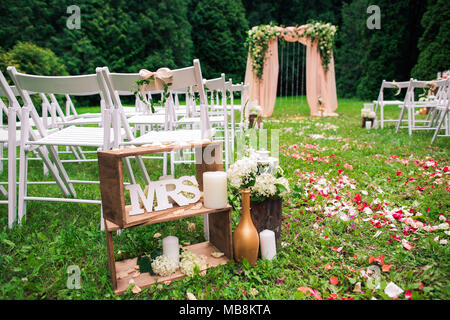 Beautiful place made with wooden square and floral roses decorations for outside wedding ceremony in green park. Rows of many empty wooden chairs read Stock Photo