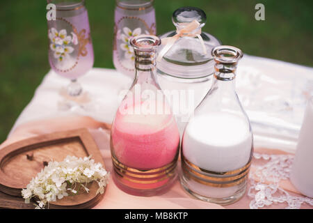 Closeup view of elements of wedding sand ceremony. Two bottles with decorative pink and white color sand ready for pouring in one vase as symbol of un Stock Photo