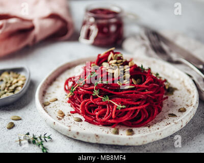 Roasted beetroot and thyme spaghetti with pumpkin seed in craft plate on gray cement background. Ideas and recipes for healthy vegan vegetarian dinner. Selective focus. Stock Photo