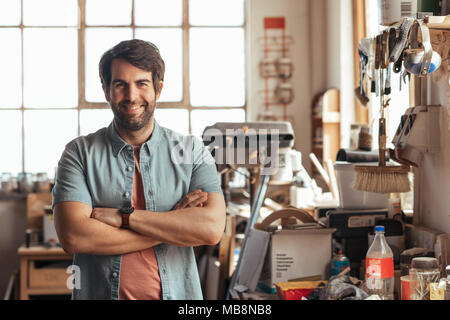 Smiling young woodworker standing by a bench in his workshop Stock Photo