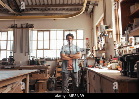 Confident young woodworker standing in his workshop full of tools Stock Photo