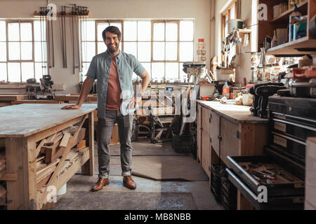 Smiling young woodworker standing by a table in his workshop Stock Photo