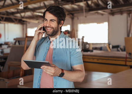 Smiling woodworker talking on his cellphone and using a tablet Stock Photo