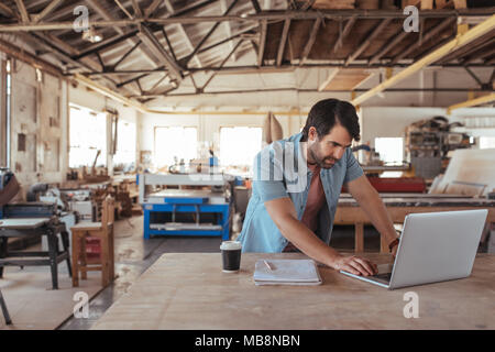 Young woodworker using a laptop in his workshop Stock Photo