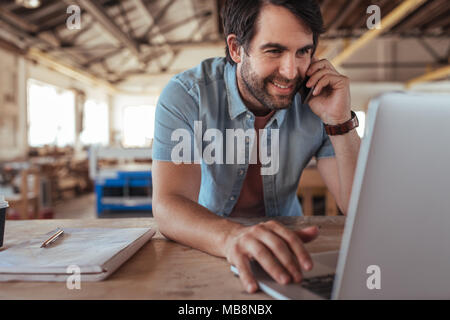 Woodworker discussing designs over the phone and using a laptop Stock Photo