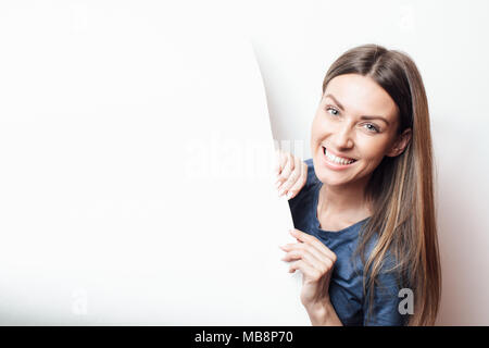 Girl holding blank banner against white background. Place for text. Photo of girl  in modern gallery and looking at the blank white canvas. Mockup Stock Photo