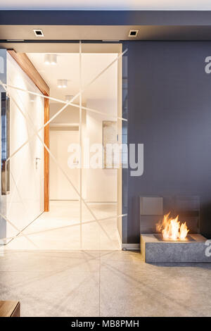 Glass, patterned door leading to a light corridor from a dark room with fireplace Stock Photo