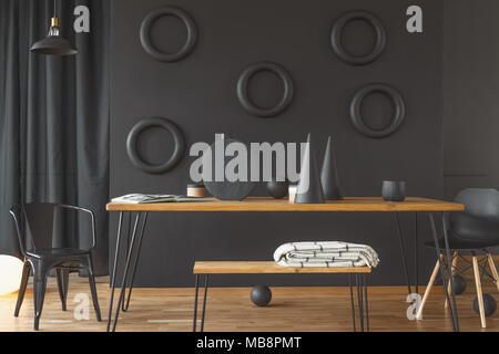 Folded white blanket placed on a bench standing by the hairpin table in minimal black dining room interior with circles on the wall Stock Photo