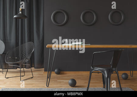 Open magazine and black vase placed on a hairpin table standing in dark dining room interior with diamond chair and three circles on the wall Stock Photo