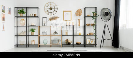 Close-up of metal racks with decorations standing against a white wall with round clock in bright living room interior Stock Photo