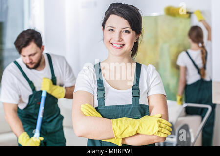 Smiling cleaning lady in a green uniform and yellow rubber gloves at work Stock Photo