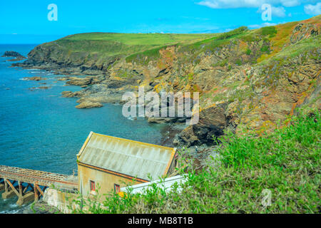 A boathouse and slipway at Lizard Point in Cornwall, over looking a bay with rocky cliffs typical of the area Stock Photo