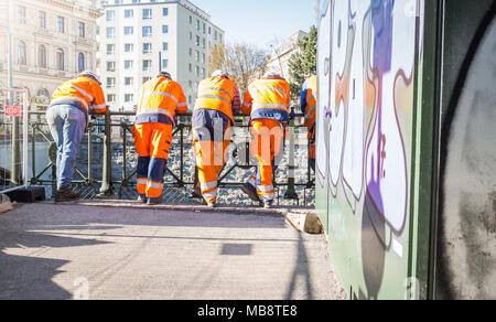 Construction workers in orange suits at a fence having a break, Vienna Austria 2-4-2018 Stock Photo