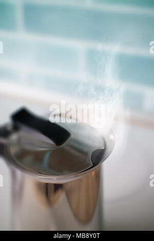 Tea kettle with boiling water against a blue tile in the kitchen Stock Photo