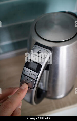 man hand click on the button iron electric kettle on the background of the kitchen Stock Photo