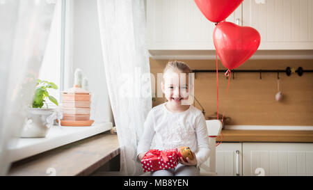 Cute preschooler girl celebrating 6th birthday. Girl holding her birthday cupcake and beautifully wrapped present, surrounded by balloons. Stock Photo