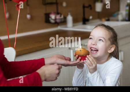 Cute preschooler girl celebrating 6th birthday. Mother giving daughter birthday cupcake with a candle. Childrens birthday party concept. Stock Photo