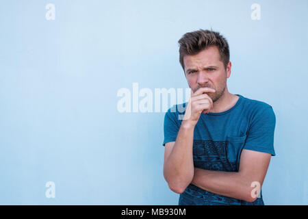 Caucasian man standing near blue wall with pensive expression on his face. Stock Photo