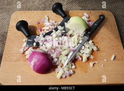 Wooden chopping board with red and white onions, a knife and slicing utensil Stock Photo