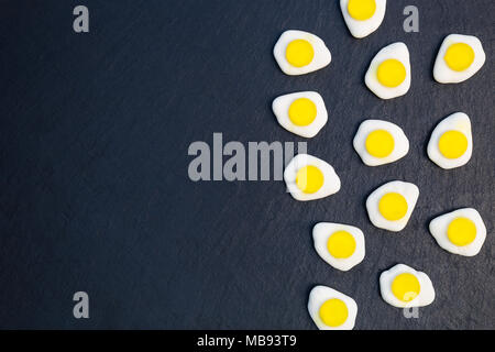 Fried eggs candy sweets overhead on dark background with copy space Stock Photo