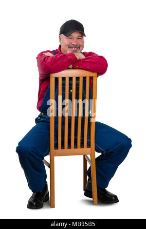 Cheerful middle class worker wearing dungarees sitting on chair against white background Stock Photo