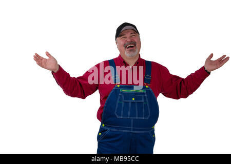 Laughing happy man in denim dungarees and a peaked cap standing raising his arms in a magnanimous gesture isolated on white Stock Photo