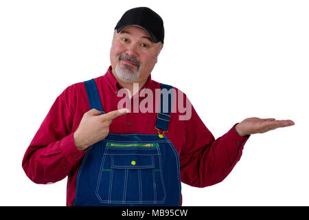 Middle-aged farmer or worker wearing a denim bi overall pointing to his empty hand over white copy space with a knowing expression of satisfaction Stock Photo