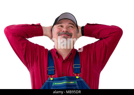 Farmer or worker in overalls and cap standing with his hands behind his head looking up with a big happy smile of satisfaction over white Stock Photo
