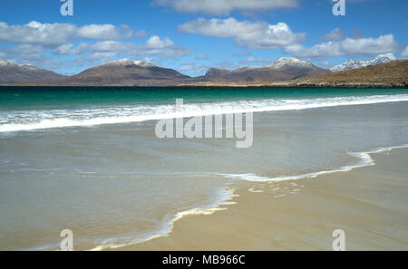 Waves rolling onto the deserted beach at Luskentyre on The Isle of Harris in spring with snow on the hills in the background. Stock Photo