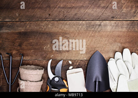 Background of various generic gardening tools, gloves and vegetable seeds shot from above over a rustic wood table in flat lay style. Stock Photo