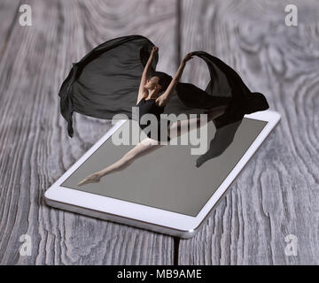 Gorgeous ballerina jumping from the phone lying on the wooden boards Stock Photo