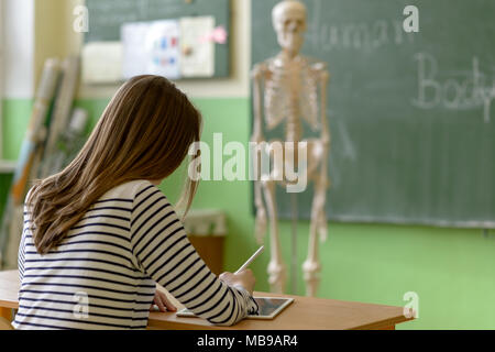 Female student writing notes using digital tablet in biology class. Generation Z Education concept. Stock Photo