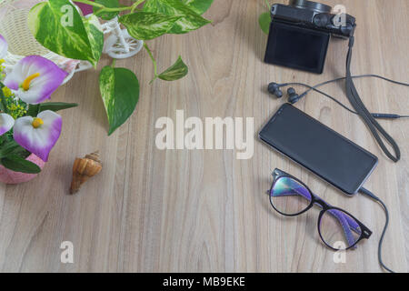 Minimal flat lay Smartphone with earphones and glasses, camera, shell,flower, green leaves on wooden table in garden with copy space, concept relaxing Stock Photo