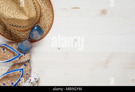 Concept of a beach holiday: slippers, sunglasses, straw hat and seashell are on a light wooden surface. Top view, flat lay Stock Photo